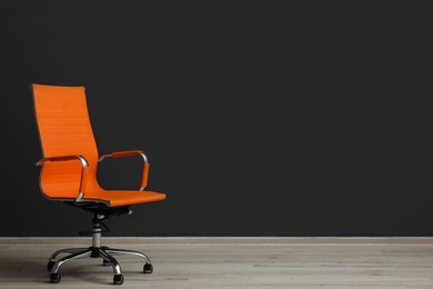 Photo of Comfortable office chair near black wall indoors. Space for text