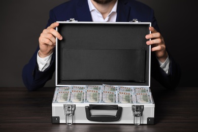 Photo of Businessman with case of dollar bills at wooden table, closeup