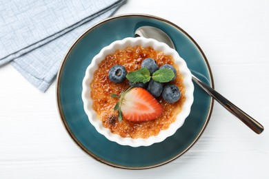 Delicious creme brulee with berries and mint in bowl on white wooden table, top view