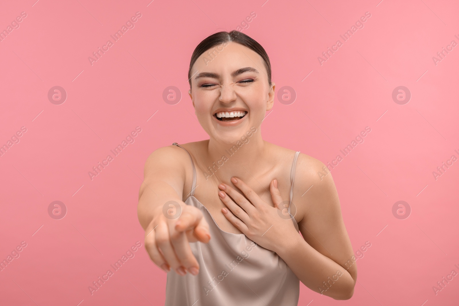 Photo of Beautiful woman pointing at something and laughing on pink background