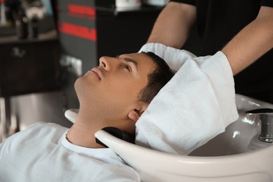 Professional barber drying client's hair with towel in salon, closeup
