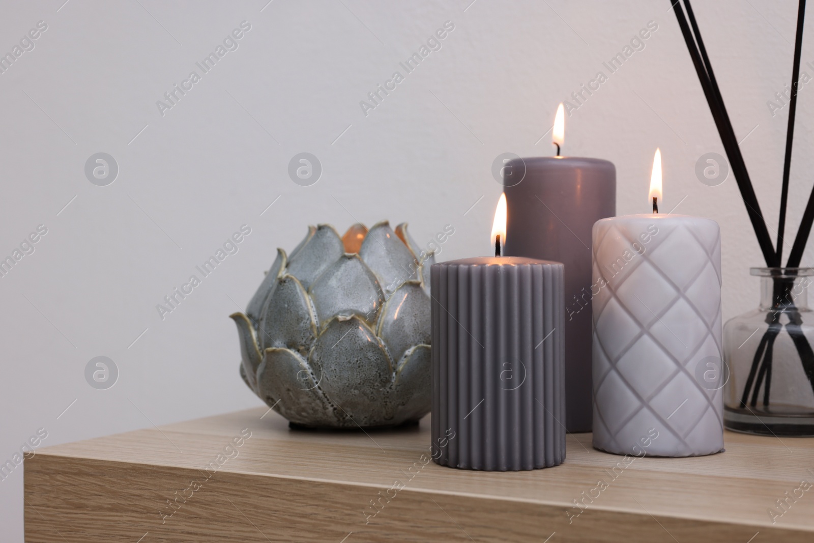 Photo of Burning candles and air freshener on wooden shelf indoors, space for text