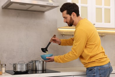 Photo of Man pouring delicious soup into bowl in kitchen