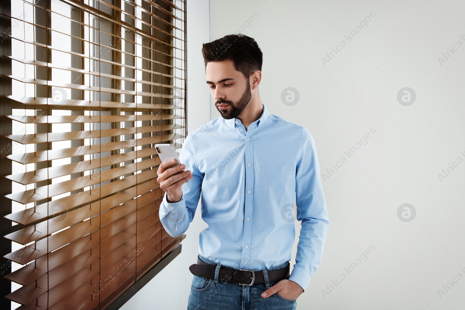 Photo of Handsome man with mobile phone at window indoors