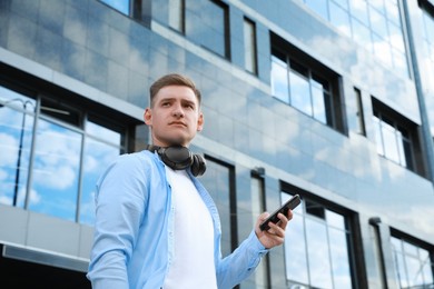 Photo of Man with headphones and smartphone near building outdoors, low angle view. Space for text