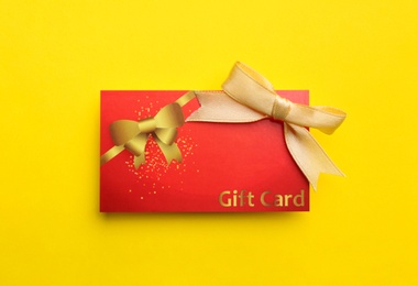 Photo of Gift card with bow on yellow background, top view