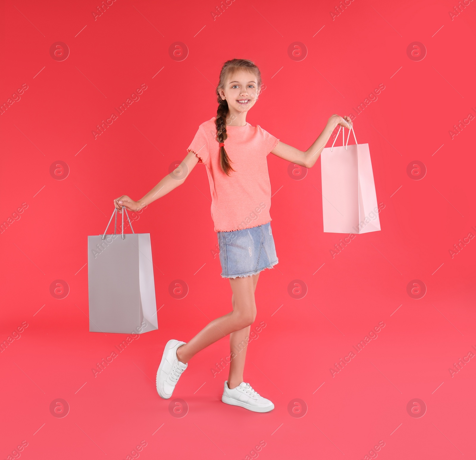 Photo of Cute little girl with shopping bags on red background
