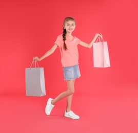 Cute little girl with shopping bags on red background