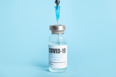 Photo of Filling syringe with coronavirus vaccine on light blue  background