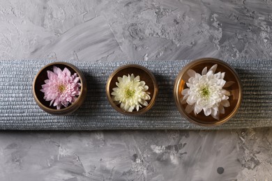 Photo of Tibetan singing bowls with water, beautiful chrysanthemum flowers on grey textured table, top view