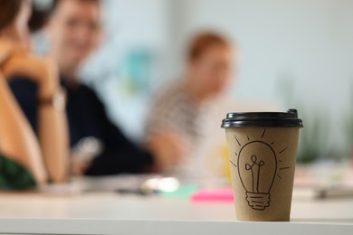 Photo of Team of employees working together in office. Paper cup of drink on white table, selective focus