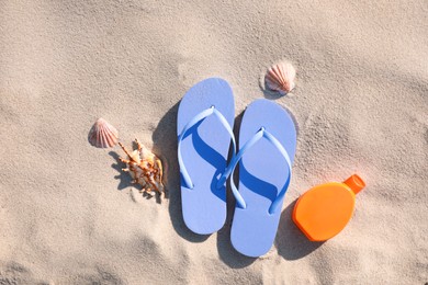 Photo of Stylish flip flops, sunscreen and sea shells on beach, flat lay