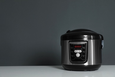Photo of Modern electric multi cooker on table against dark background. Space for text