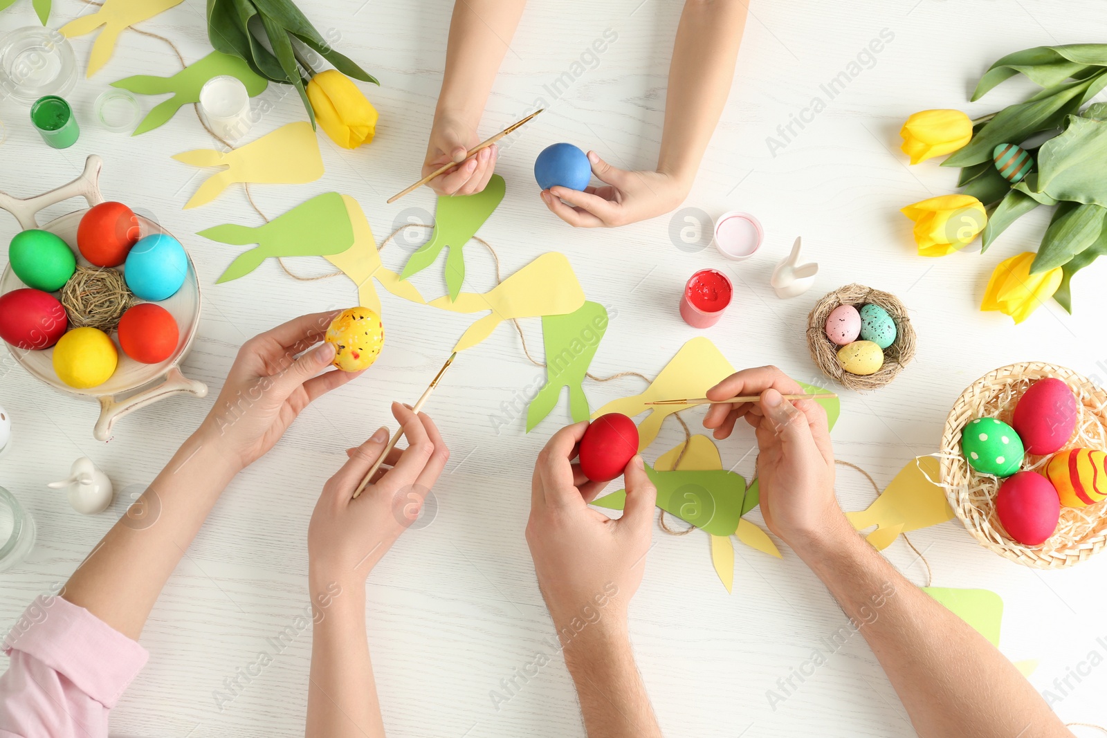Photo of Father, mother and their child painting Easter eggs at wooden table, top view