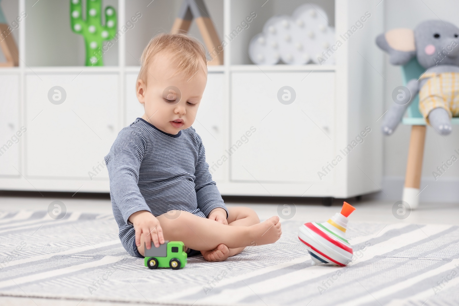 Photo of Children toys. Cute little boy playing with toy car and spinning top on rug at home