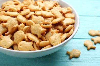 Delicious goldfish crackers in bowl on light blue wooden table, closeup