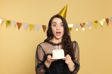 Photo of Coming of age party - 21st birthday. Surprised woman holding delicious cake with number shaped candles on beige background