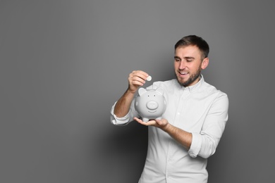 Photo of Young man putting coin into piggy bank on grey background. Space for text