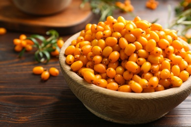 Fresh ripe sea buckthorn in bowl on wooden table, closeup