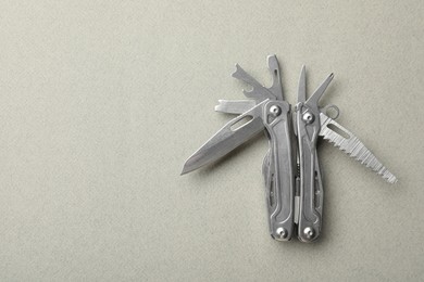 Compact portable metallic multitool on light grey background, top view. Space for text