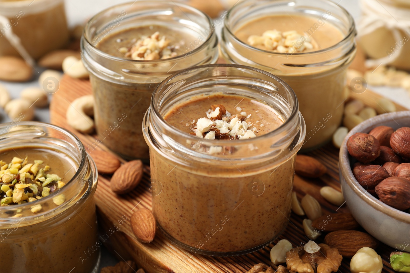 Photo of Tasty nut butters in jars and raw nuts on table, closeup