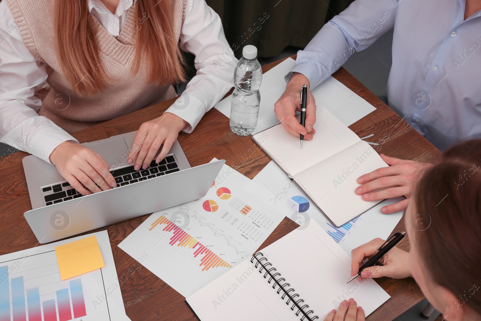 Photo of Team of employees working together at wooden table in office, above view