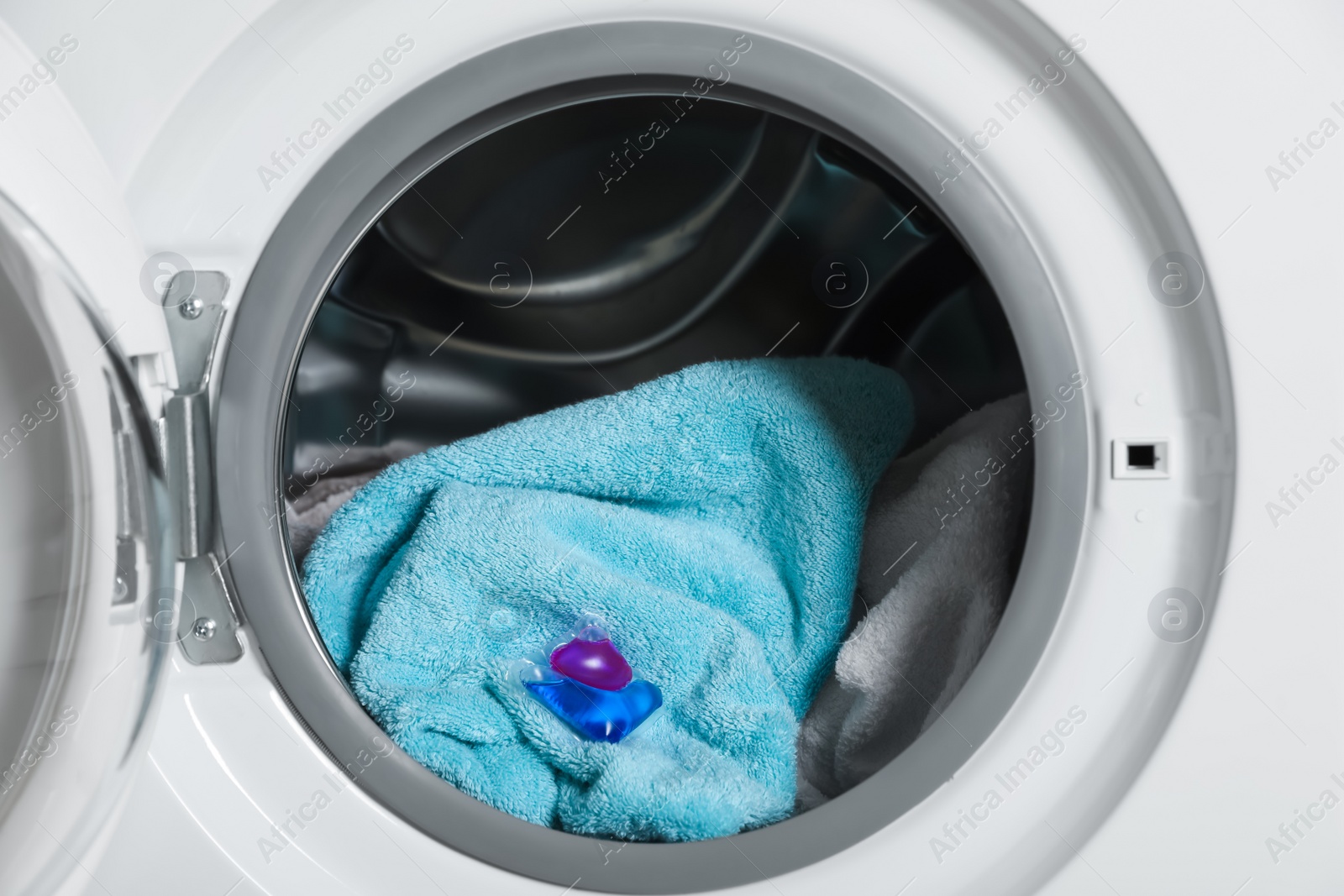 Photo of Laundry detergent capsule and towels in washing machine drum, closeup view