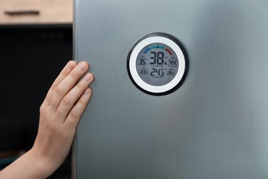Photo of Woman opening refrigerator door with digital hygrometer in kitchen, closeup