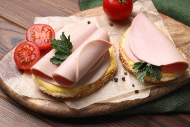 Delicious sandwiches with boiled sausage, cheese and tomatoes on wooden table, closeup