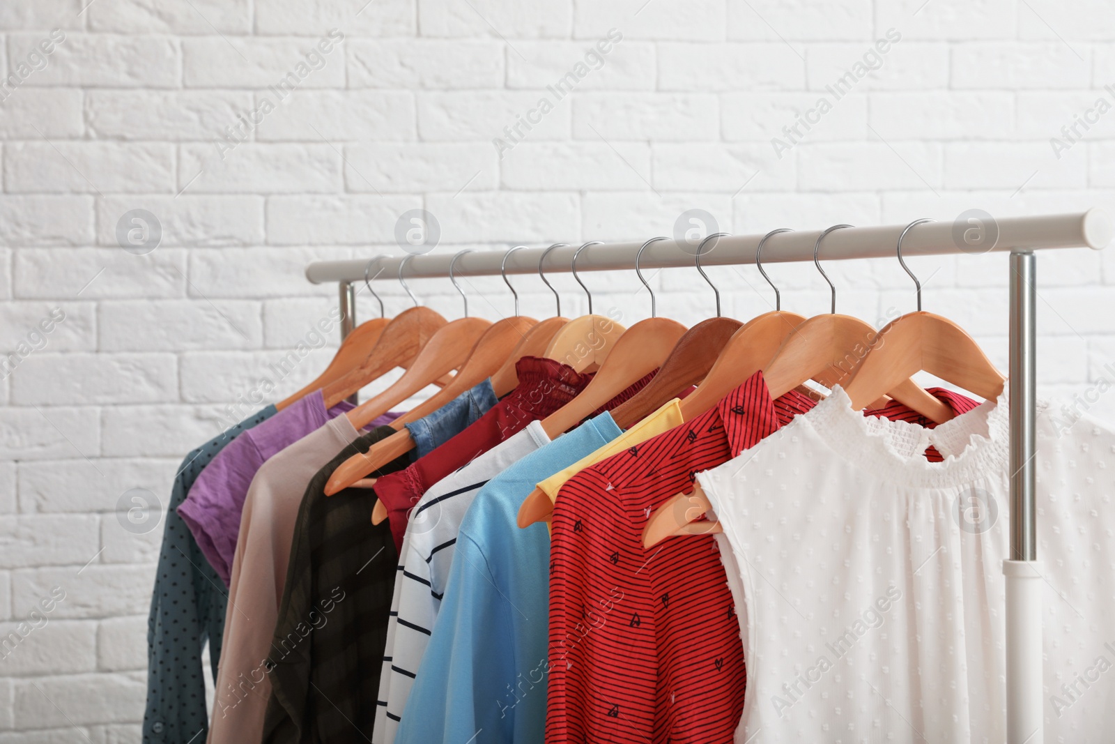 Photo of Wardrobe rack with stylish clothes near brick wall indoors