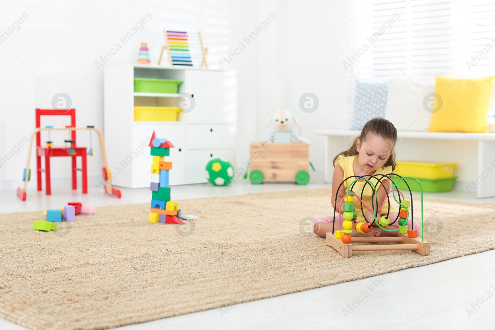 Photo of Cute little girl playing with bead maze on floor at home, space for text. Educational toy