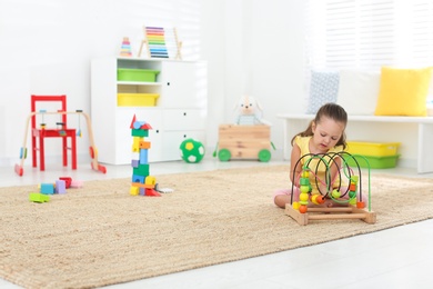 Photo of Cute little girl playing with bead maze on floor at home, space for text. Educational toy