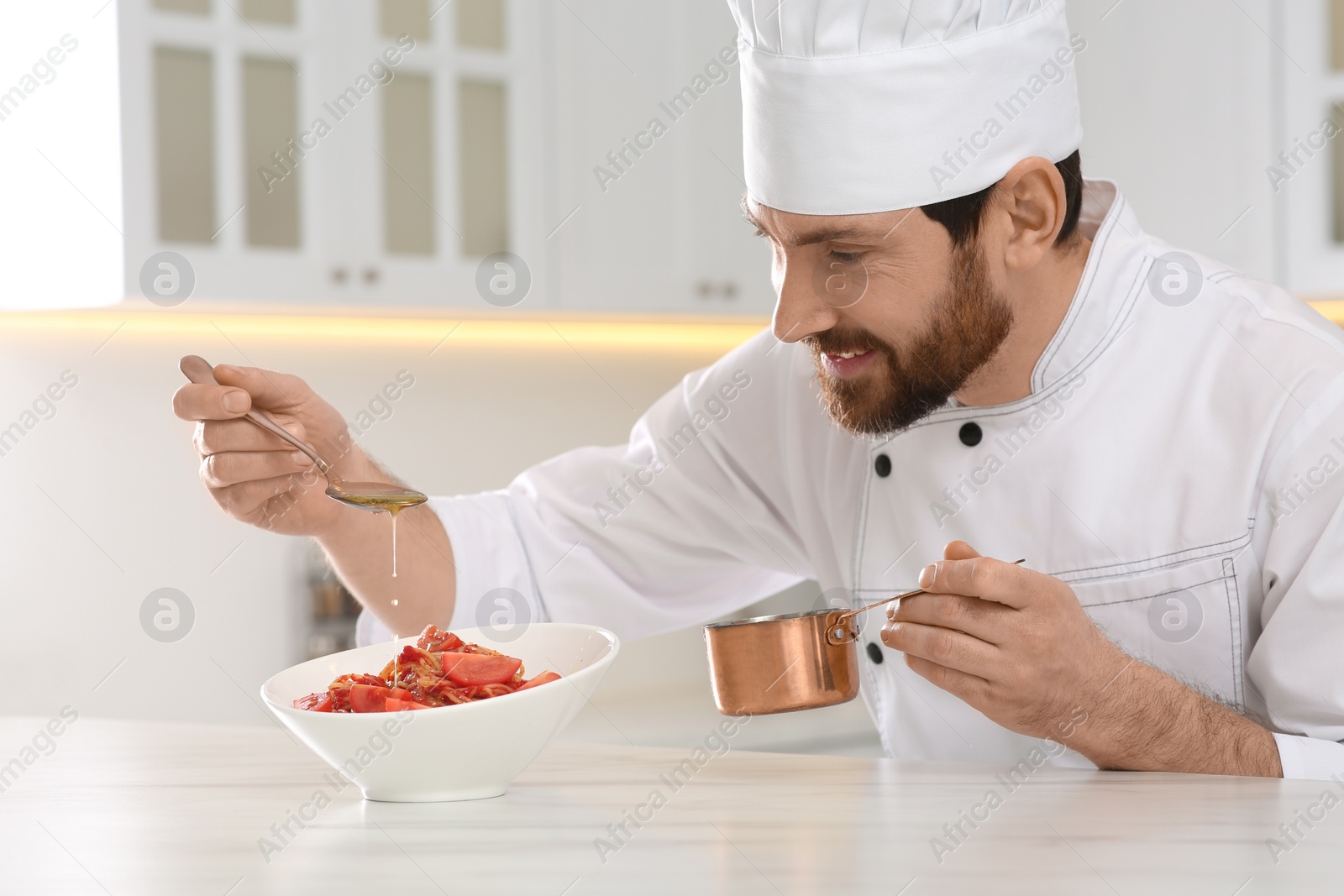 Photo of Professional chef pouring sauce into delicious spaghetti at marble table