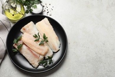 Plate with raw cod fish, parsley, oil and spices on light textured table, flat lay. Space for text