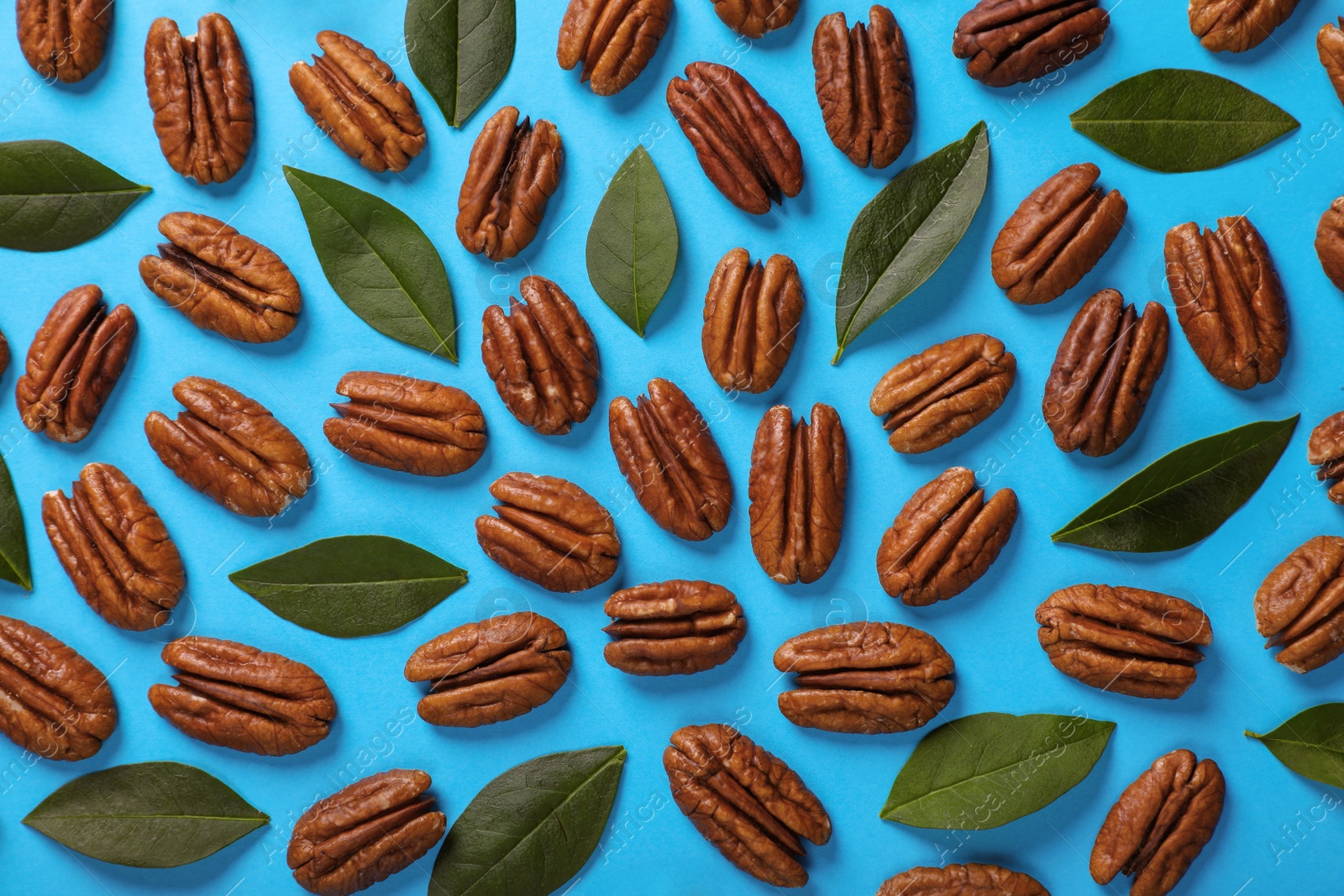 Photo of Flat lay composition with tasty pecan nuts and green leaves on light blue background
