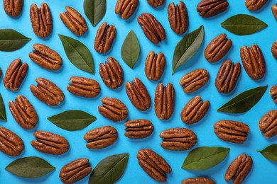 Flat lay composition with tasty pecan nuts and green leaves on light blue background