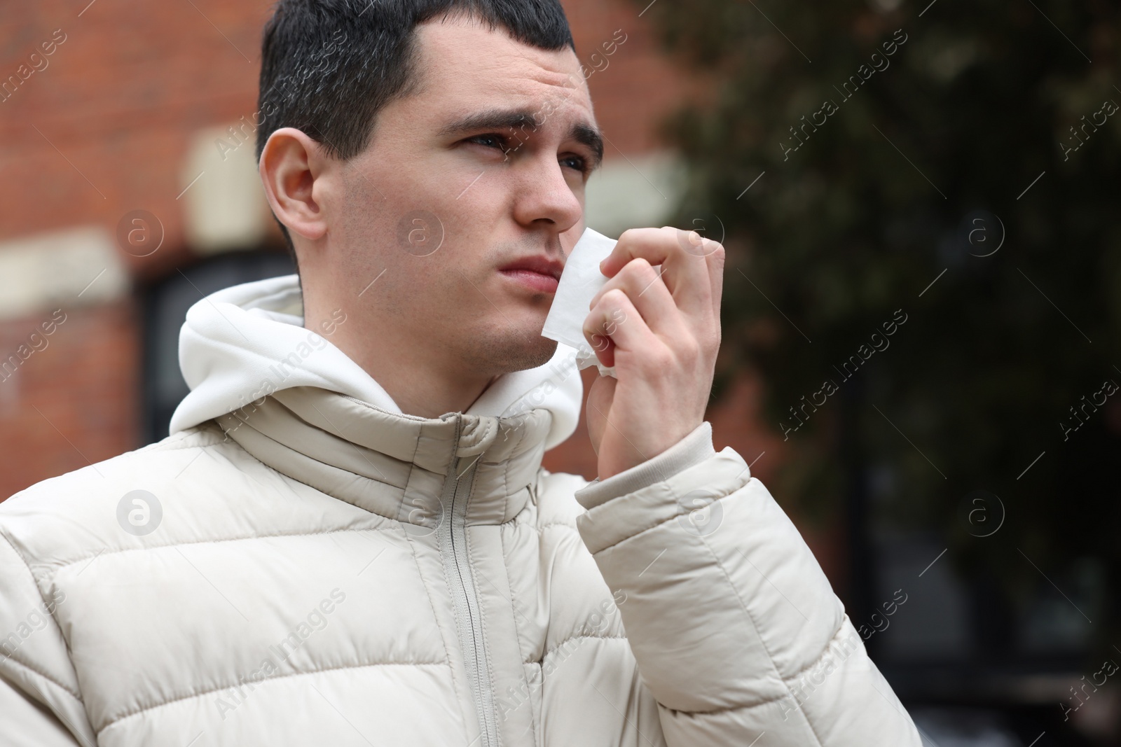 Photo of Sick young man with tissue on city street. Cold symptoms