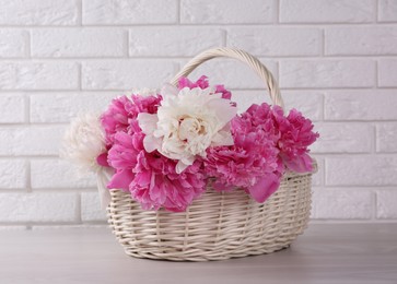 Photo of Beautiful peonies in wicker basket on white table near brick wall