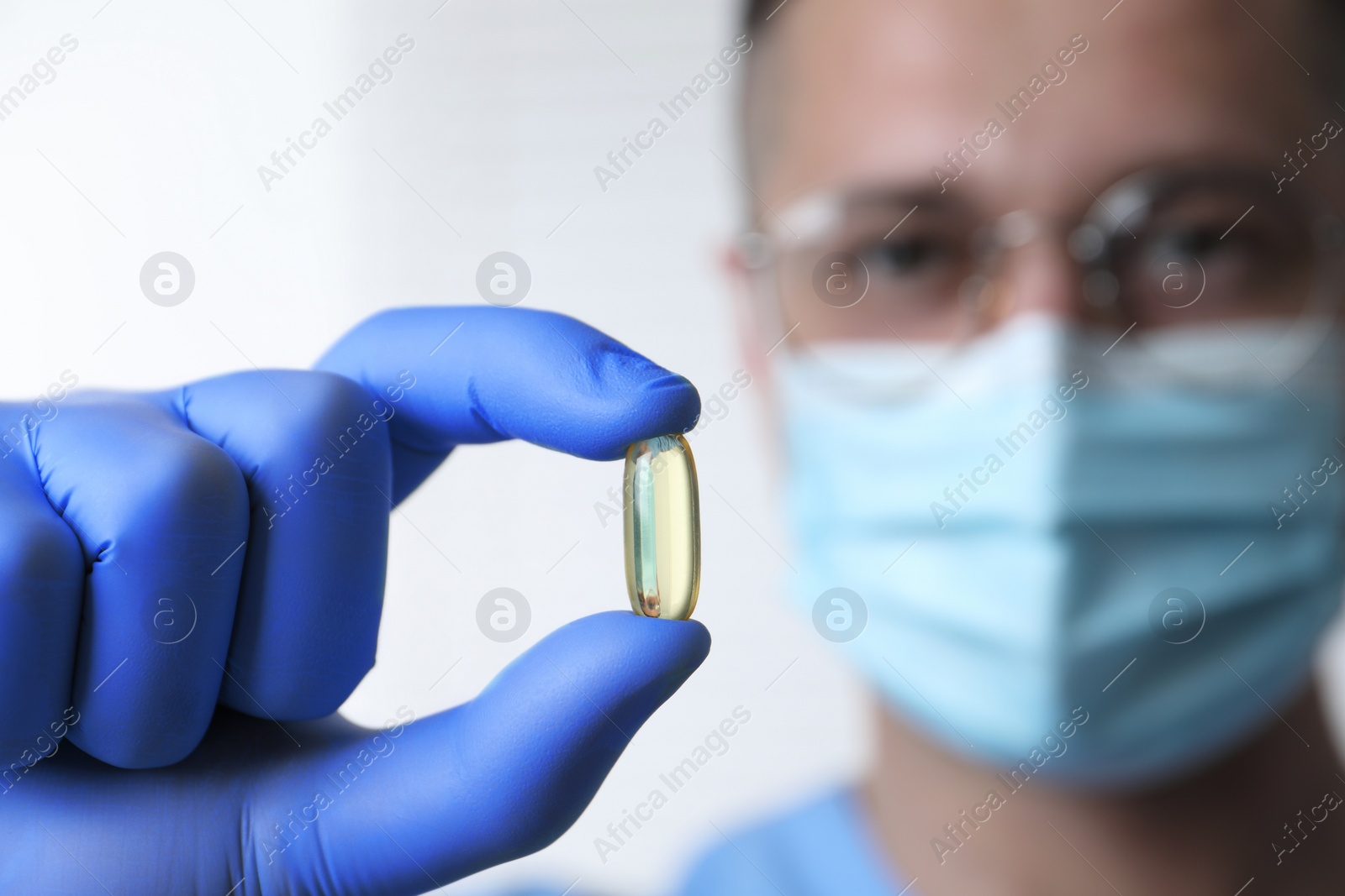 Photo of Doctor holding pill on light background, selective focus. Space for text