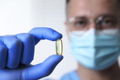 Doctor holding pill on light background, selective focus. Space for text