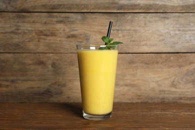 Photo of Glass of tasty smoothie with straw and mint leaves on wooden table
