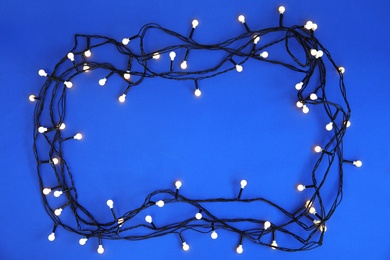 Photo of Glowing Christmas lights on color background, top view