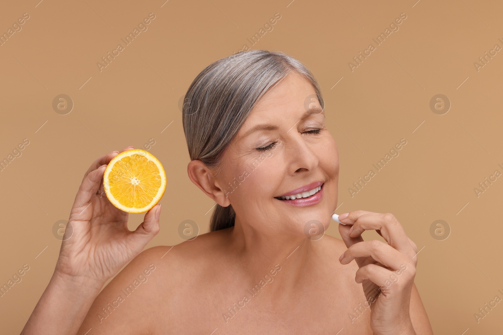 Photo of Beautiful woman with half of orange taking vitamin pill on beige background