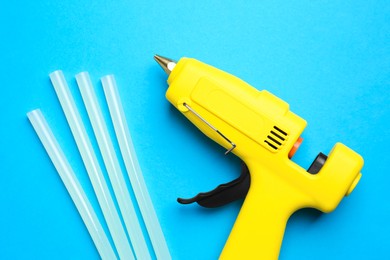 Yellow glue gun and sticks on light blue background, flat lay