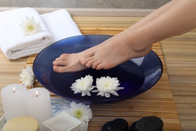 Photo of Woman soaking her feet in bowl with water and flowers on floor, closeup. Spa treatment