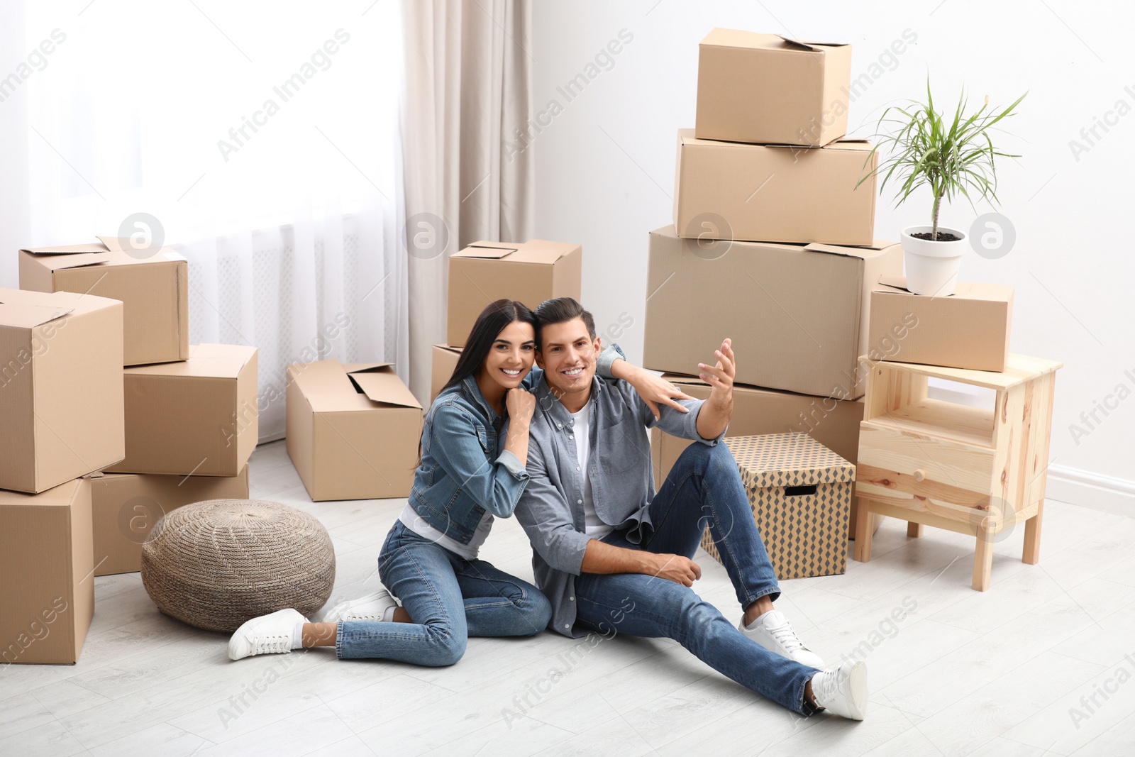 Photo of Happy couple in room with cardboard boxes on moving day