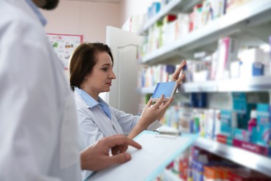 Photo of Professional pharmacists near shelves with merchandise in modern drugstore