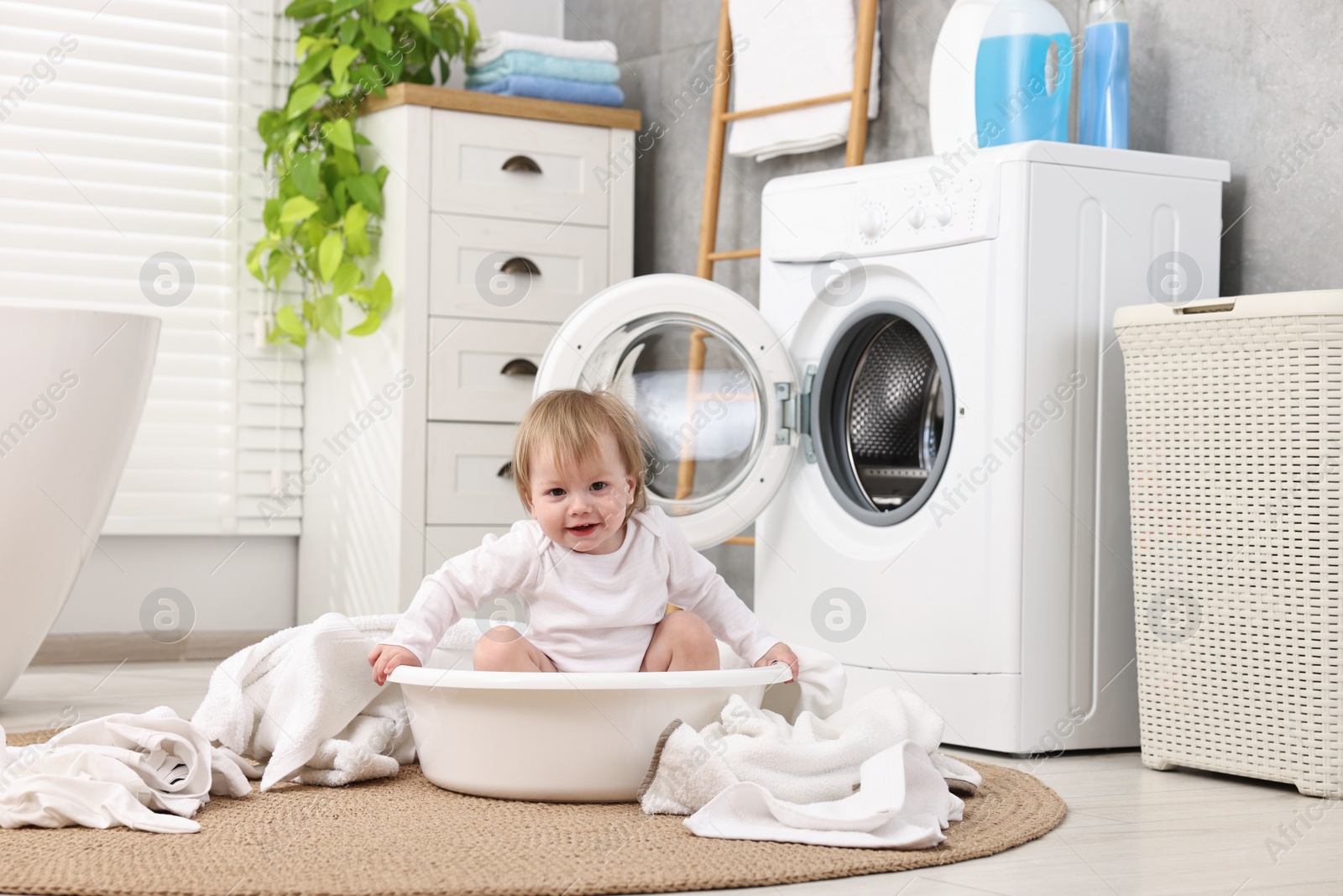 Photo of Little girl among baby clothes in bathroom