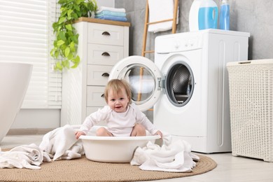 Little girl among baby clothes in bathroom