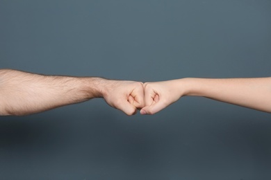 Young man and woman making fist bump on color background